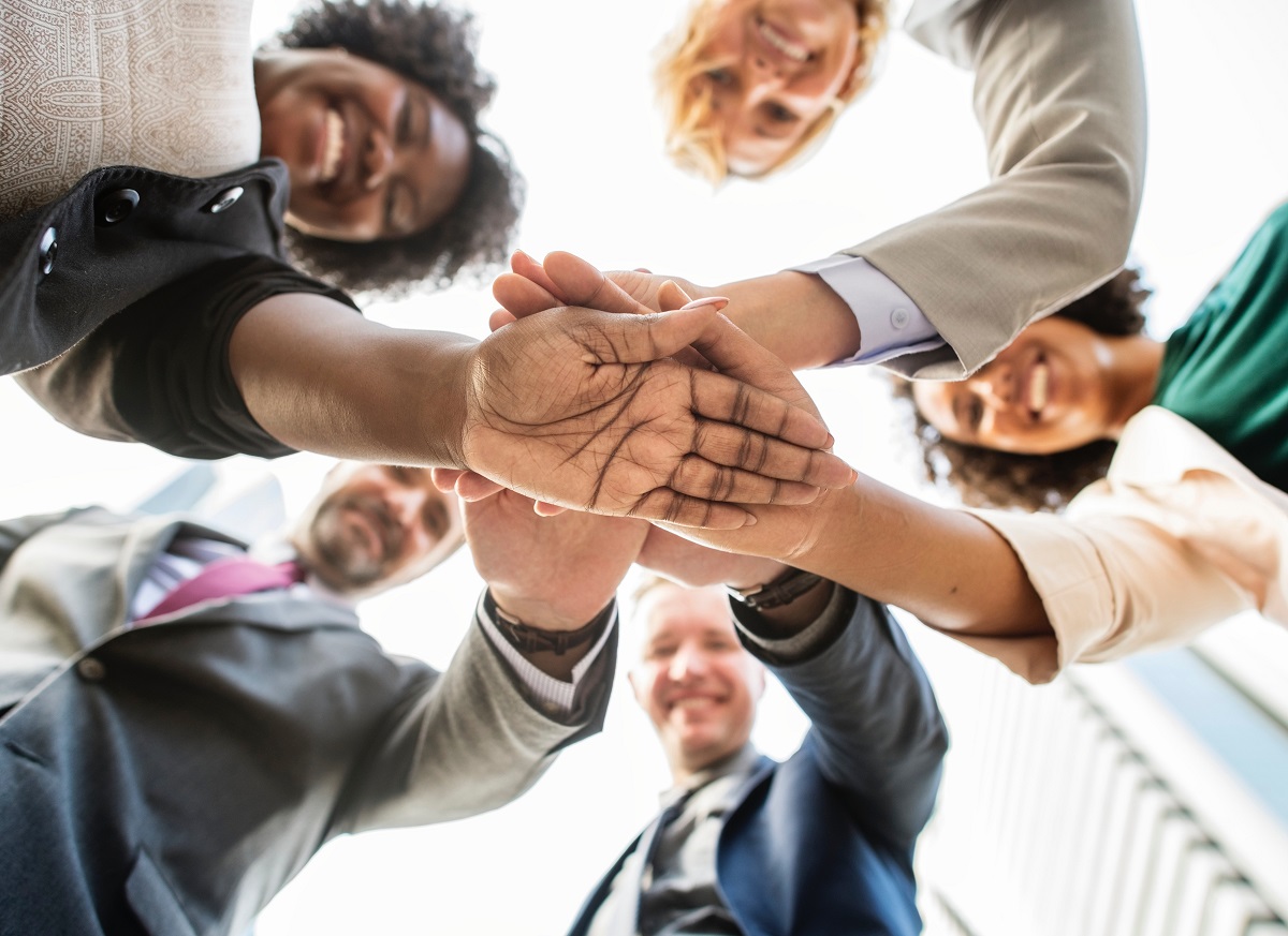 five people in a circle with one hand each in the center stacked up.