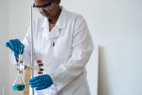 person in lab coat working with blue liquid in a beaker