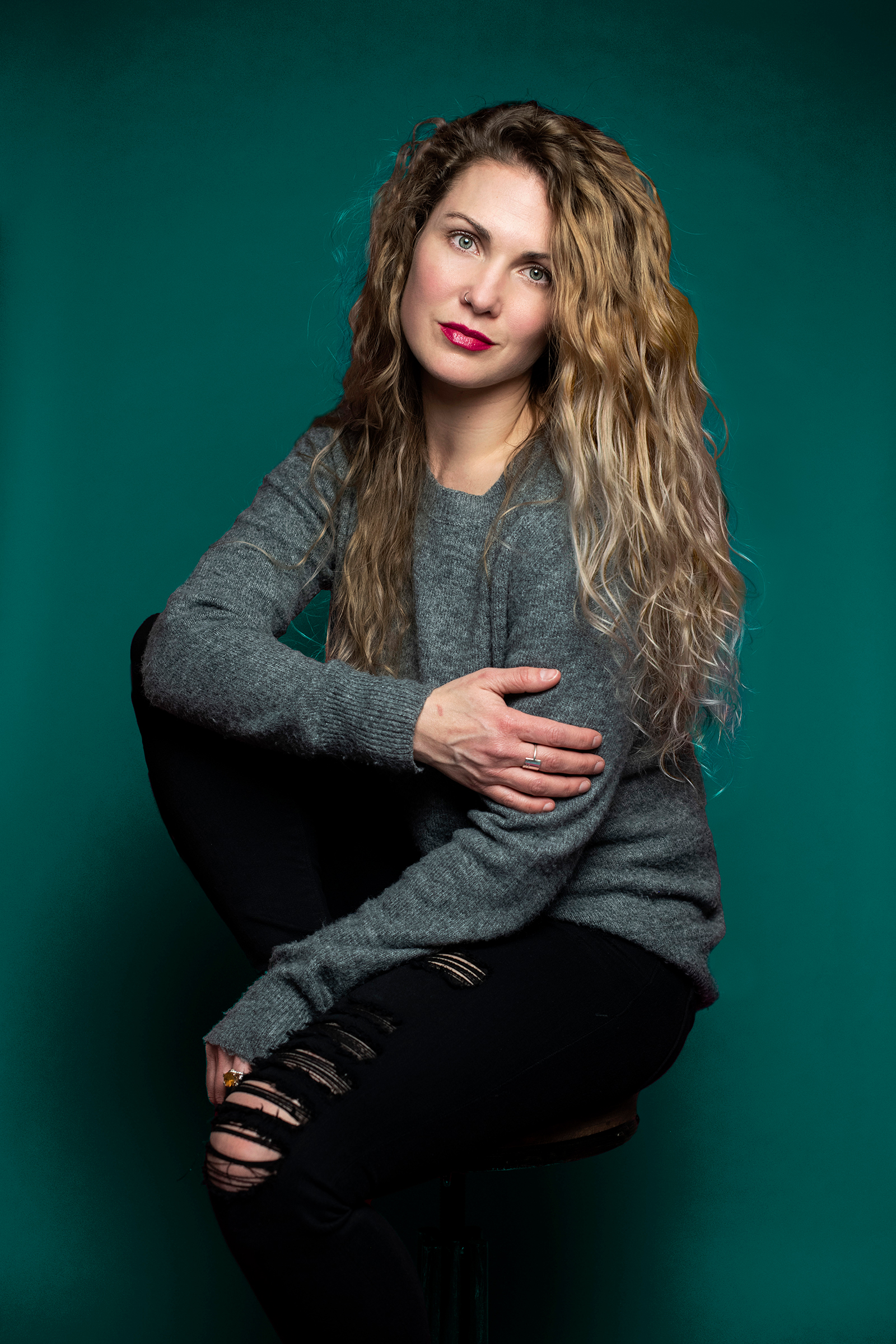 A photograph of Tara Mesyn crouching in front of a green backdrop.