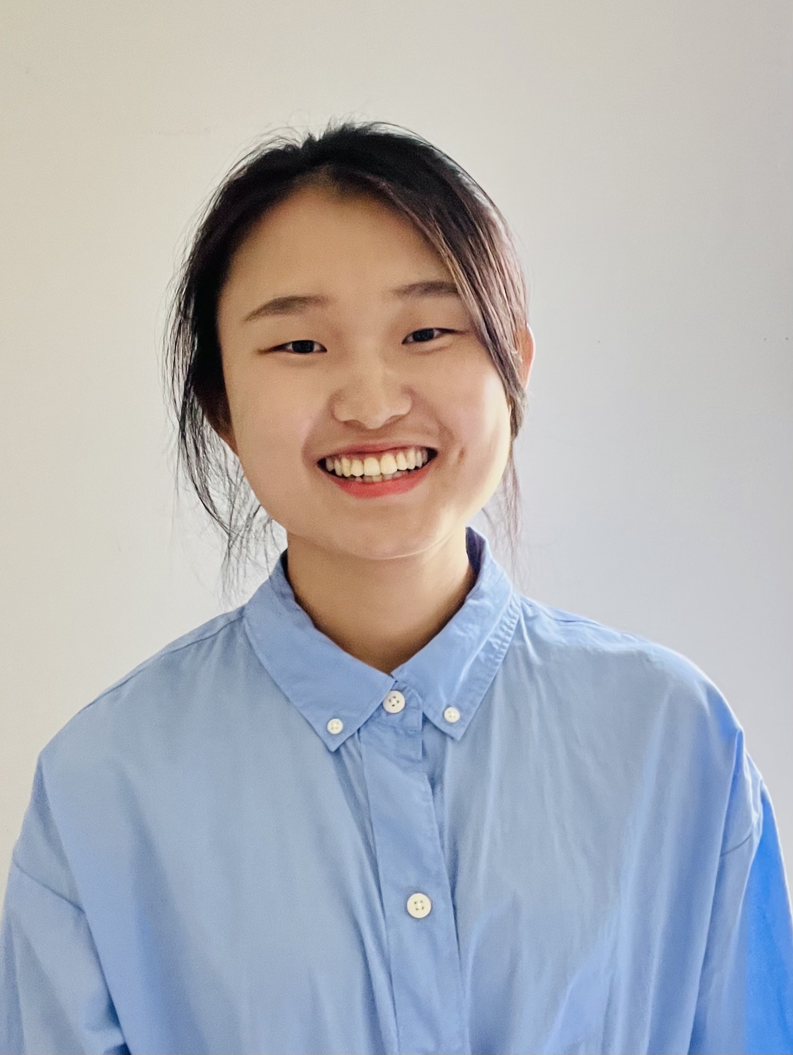 Qi Huang in a pale blue shirt on a tan background.