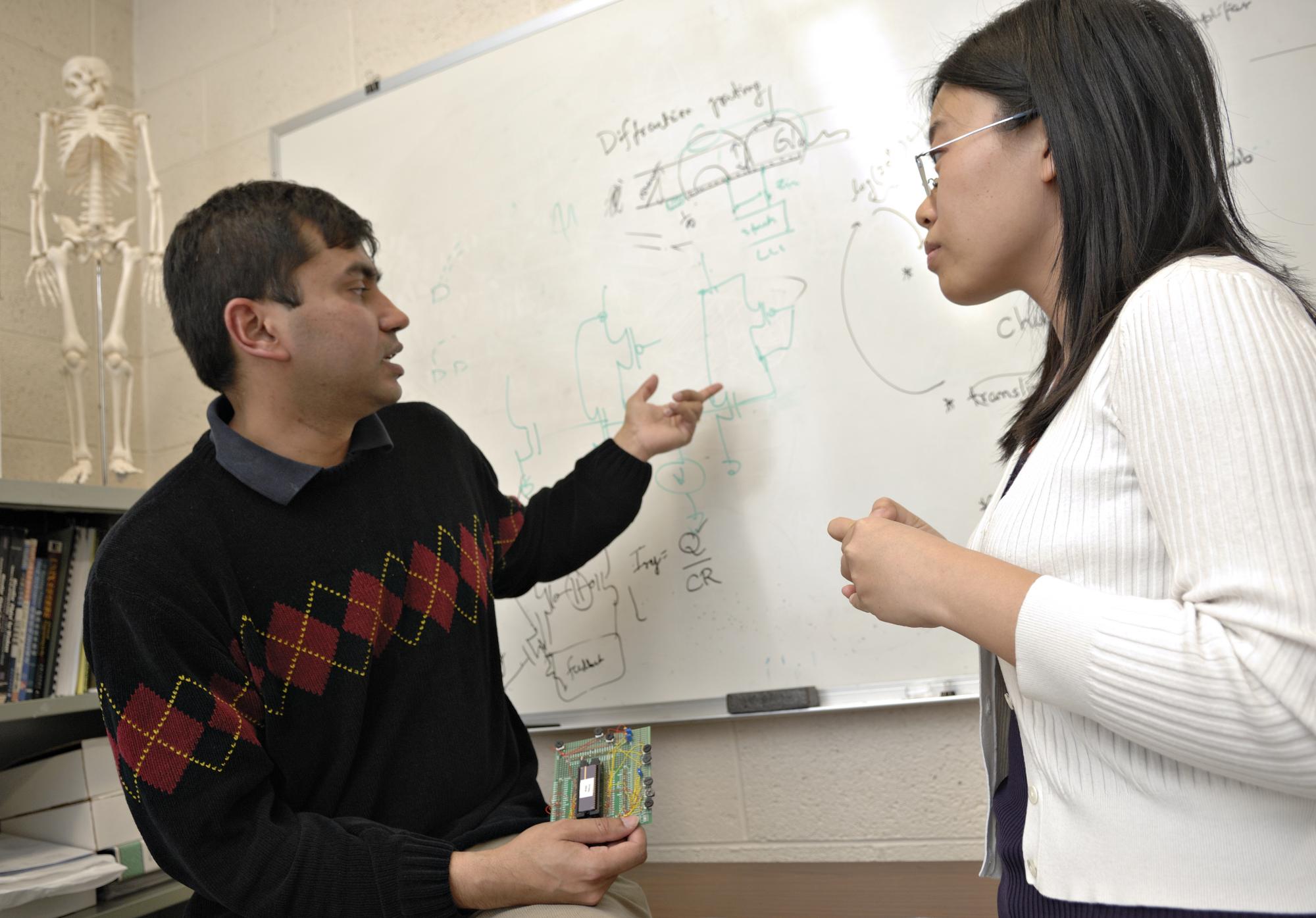 Two people reviewing a problem on a whiteboard.