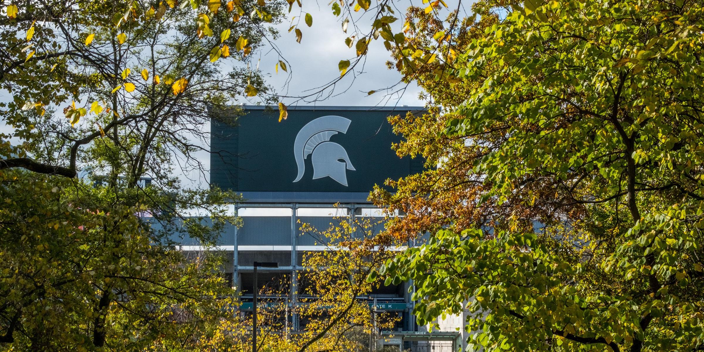 A green billboard with a white Spartan helmet, flanked by autumn foliage.