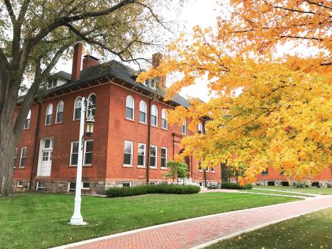 A red brick building sitting behind a tree with orange leaves.